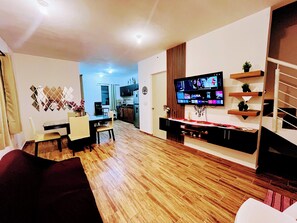 Ein modernes Wohnzimmer mit Flachbildfernseher, Holzböden und einem Essbereich mit Tisch und Stühlen.