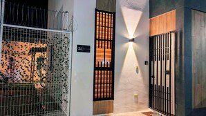 A hallway with a metal gate, a lit wall-mounted light fixture, and a number sign indicating room 26.