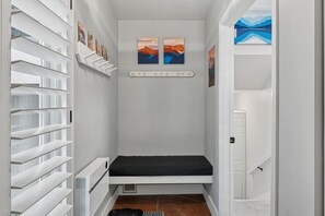 A narrow hallway with a black bench, white shelving units, and two paintings on the wall. - EagleVail Alpine Retreat | Pool, Golf & Pickleball (Avon)