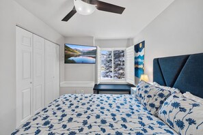 Una camera da letto con un letto, una ventola a soffitto, una televisione e una finestra vista alberi coperti di neve.
