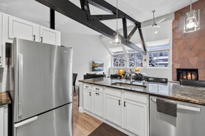 A modern kitchen with a stainless steel refrigerator, white cabinets, a granite countertop, and a stone fireplace. - EagleVail Alpine Retreat | Pool, Golf & Pickleball (Avon)