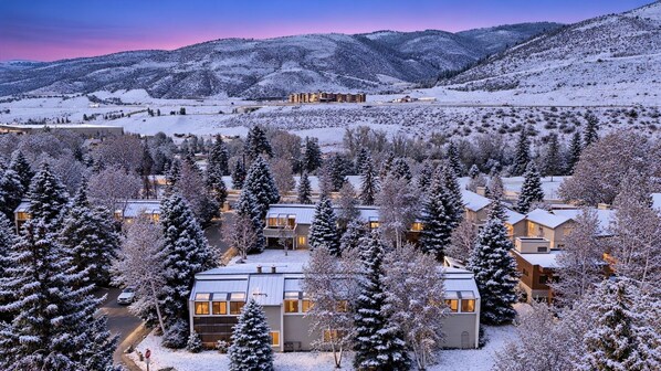 Zona residenziale innevata con diverse case, un edificio importante sullo sfondo e cielo sereno.