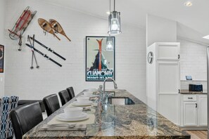 A modern kitchen with a granite countertop, white cabinetry, and a dining area with a long table set for four. - EagleVail Alpine Retreat | Pool, Golf & Pickleball (Avon)