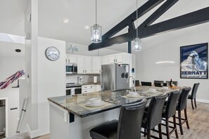Una cucina moderna con mobili bianchi, un frigorifero in acciaio inossidabile e un'area pranzo con un piano in marmo e sedie nere.