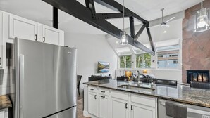 A modern kitchen with a stainless steel refrigerator, white cabinetry, a granite countertop, and a stone accent wall. - EagleVail Alpine Retreat | Pool, Golf & Pickleball (Avon)