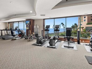 A gym with treadmills, elliptical machines, and weight equipment, with a view of the ocean through large windows. - Beachfront 3BR/2BA condo in Marco Island with pool, wifi, and ocean views. (Marco Island)