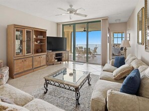 A living room with a television, a sofa, a coffee table, and a balcony with outdoor furniture. - Beachfront 3BR/2BA condo in Marco Island with pool, wifi, and ocean views. (Marco Island)