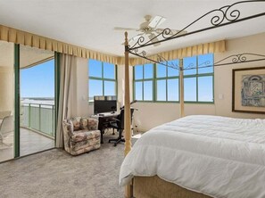 A hotel room with a bed, a desk, a chair, a ceiling fan, and a large window. - Beachfront 3BR/2BA condo in Marco Island with pool, wifi, and ocean views. (Marco Island)
