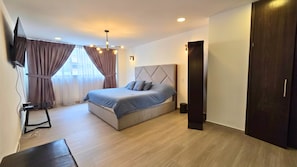 A modern bedroom with a bed, curtains, a TV, and a wooden floor. - Residencia Élite Polanco | Corporate (Mexico City)