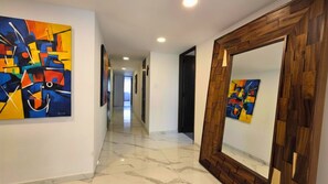 A corridor with artwork on the walls, a wooden-framed mirror, and a tiled floor. - Residencia Élite Polanco | Corporate (Mexico City)