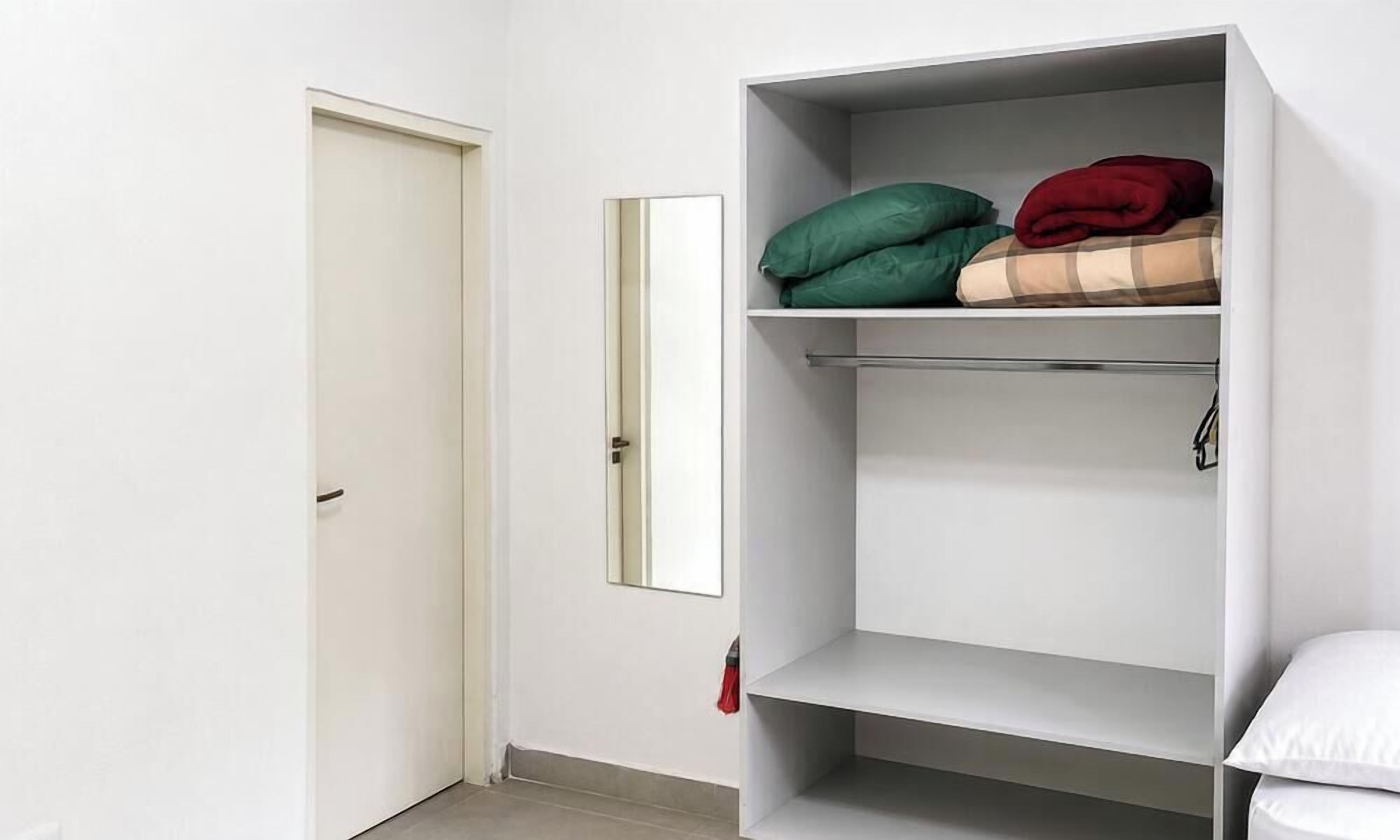 A room with a white door, a mirror, and a white wardrobe with shelves.
