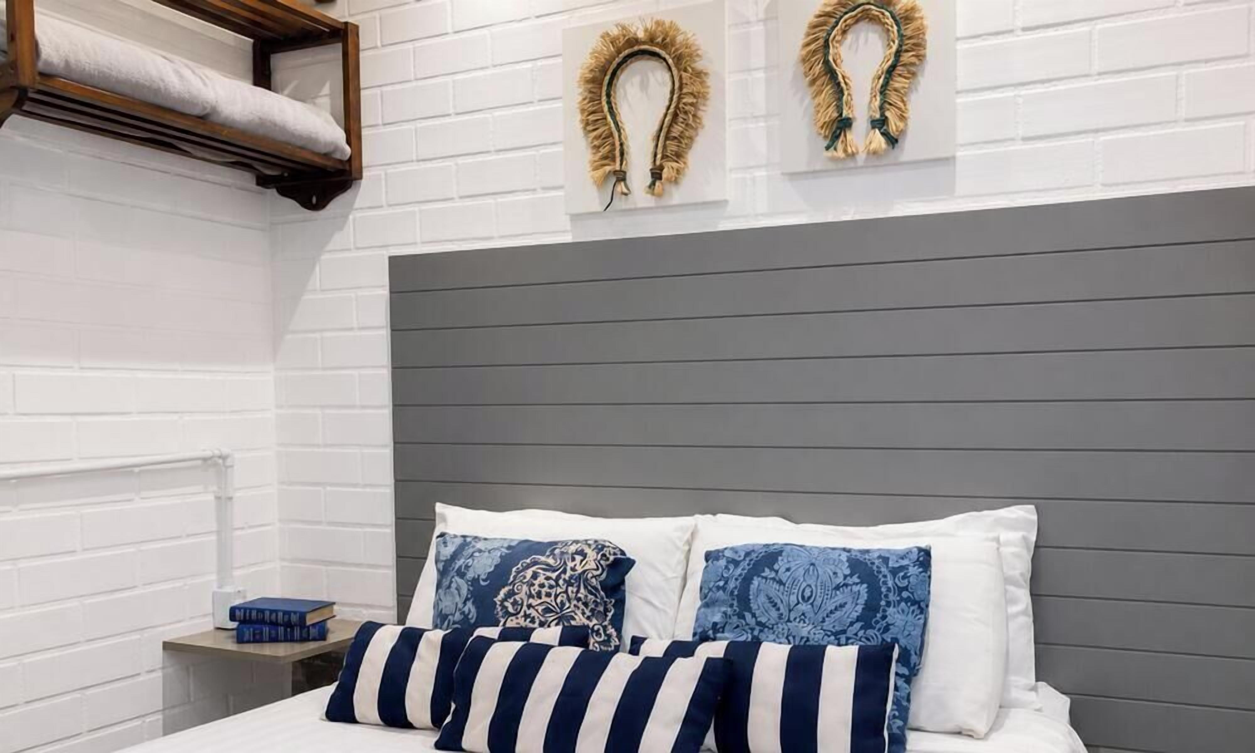 Quarto com cama, almofadas, mesa de cabeceira e prateleira na parede.