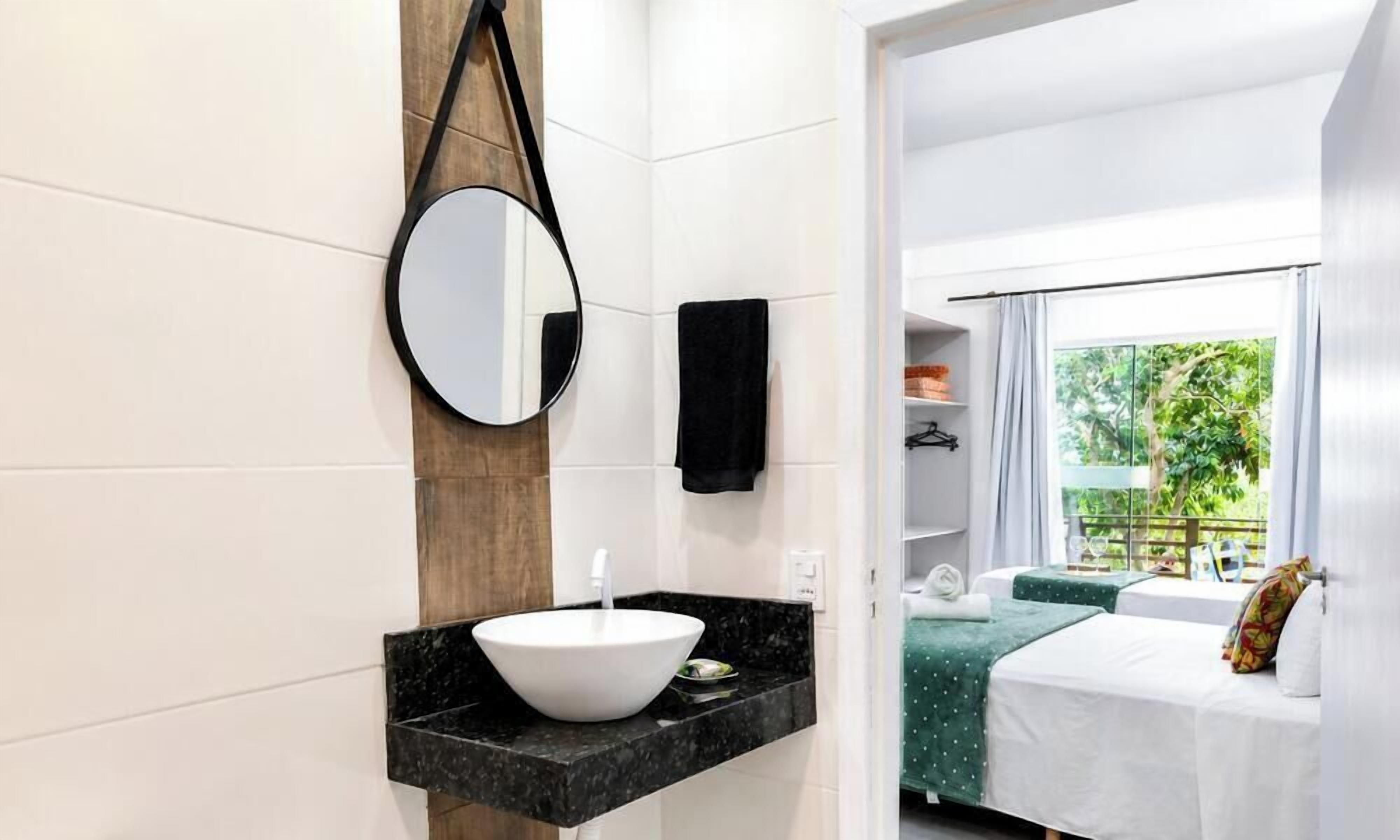 Un baño moderno con un lavamanos blanco, un espejo redondo y una pared de madera decorativa.