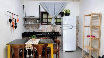 A compact kitchen with a refrigerator, a dining table with chairs, and a small shelf unit.