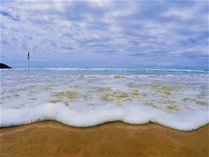 A beach with waves lapping at the shore and a flag in the distance.