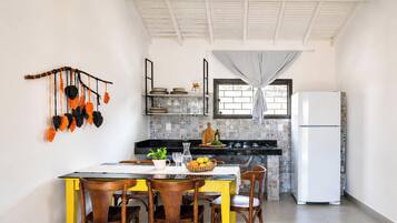 Cocina compacta con comedor, que cuenta con un salpicadero de azulejos, un refrigerador blanco y una planta decorativa colgante.