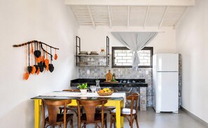 A compact kitchen with a dining area, featuring a tiled backsplash, a white refrigerator, and a hanging plant decoration.