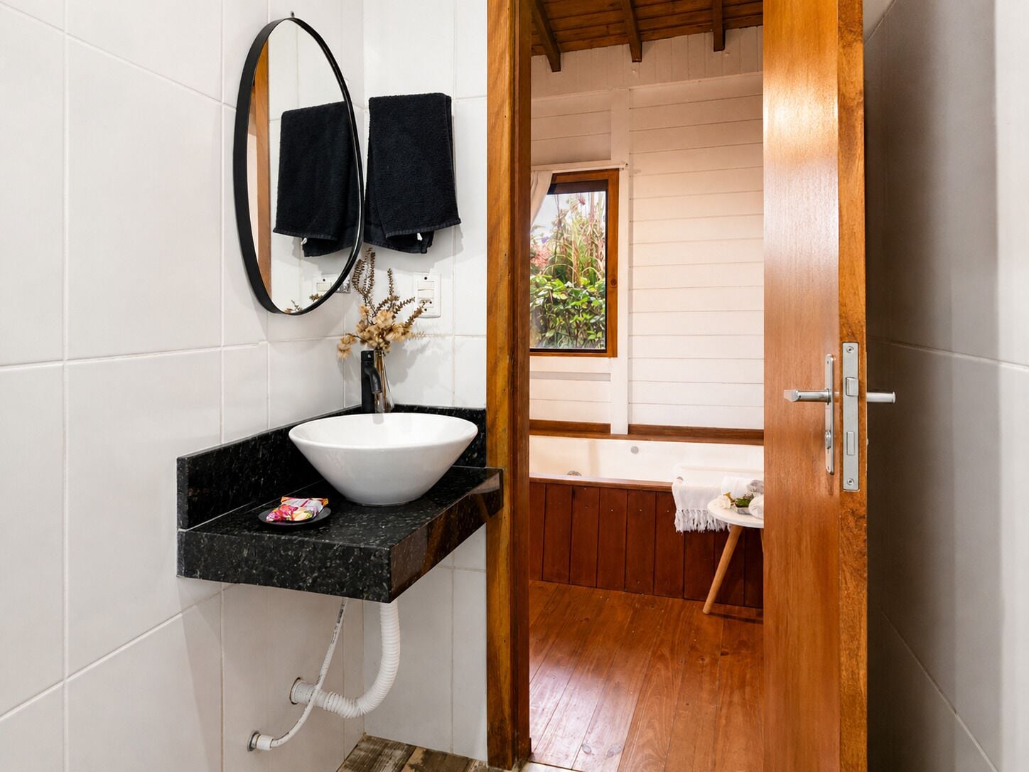 Un baño con lavamanos blanco, encimera negra y una puerta de madera que da a la zona de la ducha.