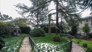 Un sendero de piedra que atraviesa un jardín con plantas cubiertas de nieve, rodeado de árboles y una cerca.