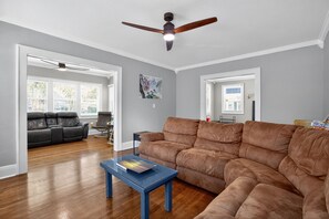 A living room with a brown leather sofa, a blue coffee table, and a ceiling fan.