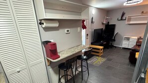 Ett kompakt kök med en arbetsbänk, en kaffemaskin, en tv och en sittgrupp med pallar.