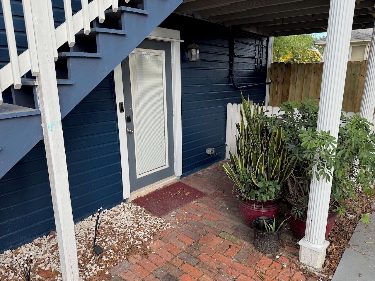 A covered porch with a staircase, a door, and potted plants.