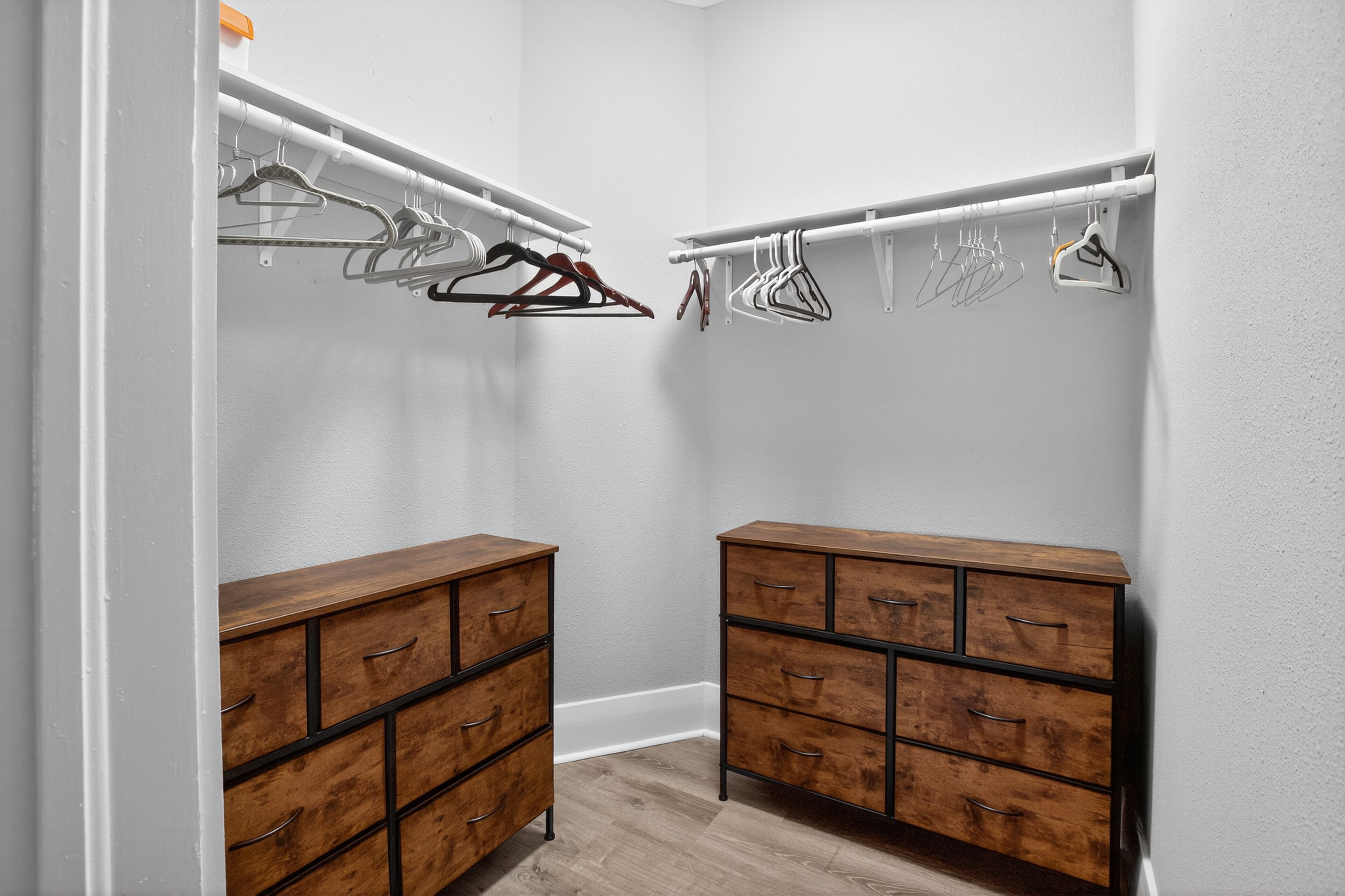 Een inloopkast met twee houten kasten en een kledingroede met kleding.