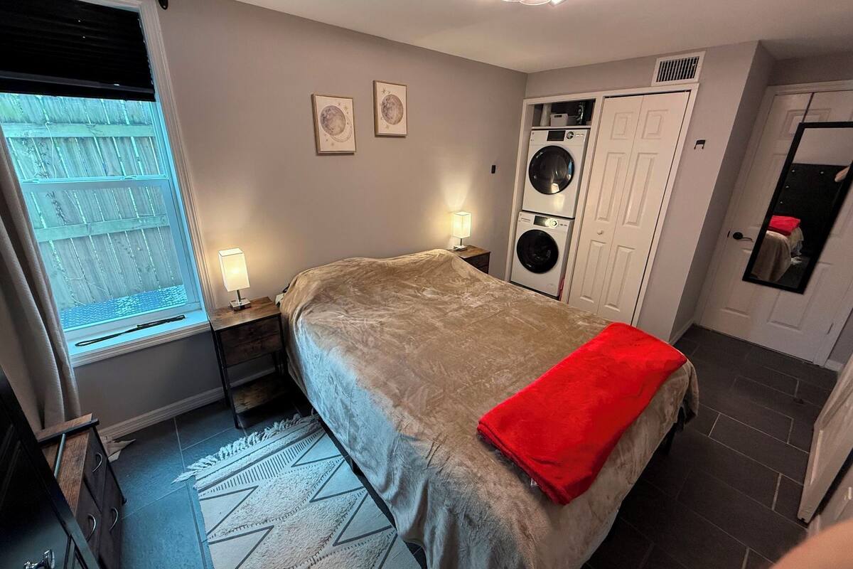 Quarto com cama, janela, máquina de lavar e espelho.