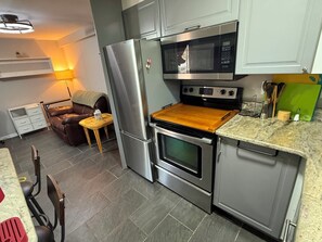 A compact kitchen with a refrigerator, microwave, oven, and a wooden countertop.