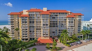 A multi-story hotel with balconies, a parking area, and palm trees. - Beachfront 1BR condo with pool, WiFi, and Gulf views. (Marco Island)