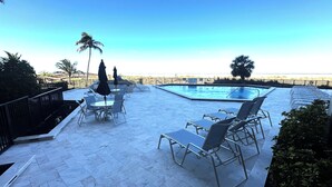 A pool area with lounge chairs and tables, a clear sky, and a view of the beach. - Beachfront 1BR condo with pool, WiFi, and Gulf views. (Marco Island)