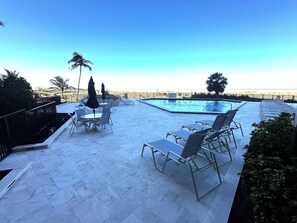 A pool area with lounge chairs and tables, a clear sky, and a view of the beach. - Beachfront 1BR condo with pool, WiFi, and Gulf views. (Marco Island)