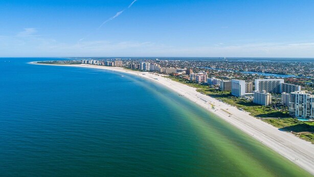 A coastal cityscape with a long sandy beach, high-rise buildings, and a clear blue sky. - Beachfront 1BR condo with pool, WiFi, and Gulf views. (Marco Island)