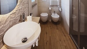 Un baño con un lavabo ovalado grande, dos lavamanos redondos, una cabina de ducha de vidrio y una pared de acento de piedra.