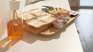 Bandeja de desayuno con pan, mantequilla, mermelada y una botella de té THD sobre una mesa.