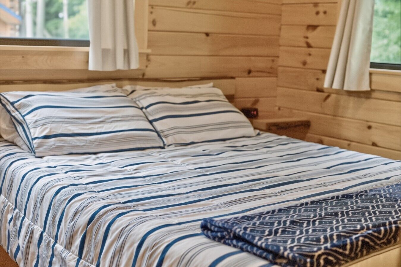 Une pièce aménagée comme un chalet en bois, avec un lit, une literie à rayures et un plaid à motifs.