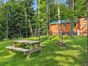 A picnic table in a grassy area with a hammock and a small fire pit. - Middlebury Center Cabins w Pond, Trails & Views! (Middlebury Center)