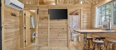 A wooden cabin interior with a kitchen area, bar stools, and a TV.