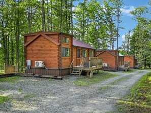A row of log cabins with wooden decks and air conditioning units, surrounded by a forest. - Middlebury Center Cabins w Pond, Trails & Views! (Middlebury Center)