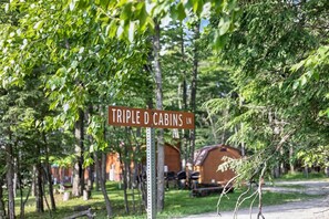 A sign for Triple D Cabins LN, surrounded by trees and cabins. - Middlebury Center Cabins w Pond, Trails & Views! (Middlebury Center)
