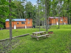 En stuga med ett blått tak, omgiven av en gräsyta med ett picknickbord och en eldstad.