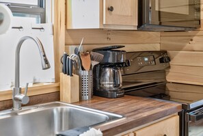 A kitchen with a stainless steel sink, a coffee maker, and wooden cabinets. - Middlebury Center Cabins w Pond, Trails & Views! (Middlebury Center)