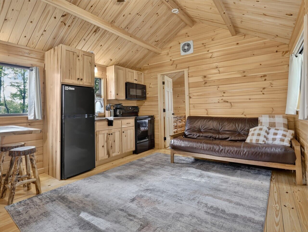 Una cabaña de madera con cocina, un sofá de cuero marrón y una zona de comedor.