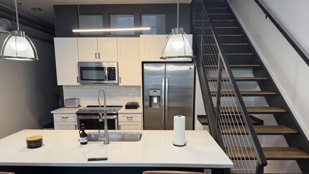 Eine moderne Küche mit Edelstahlgeräten, einer zentralen Kochinsel und einer Treppe.