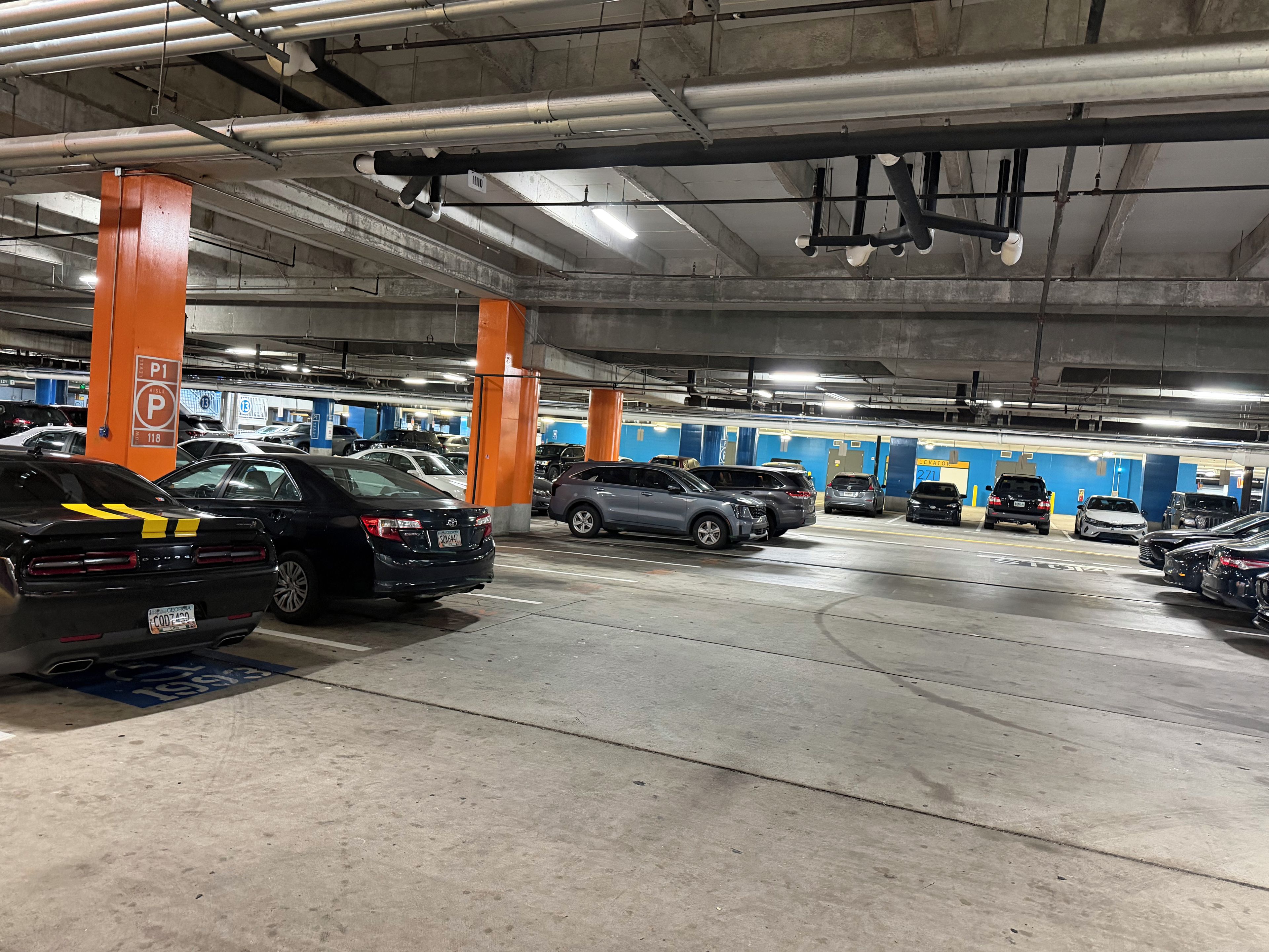 Un parking souterrain à plusieurs niveaux, avec des voitures garées dans des emplacements désignés, des piliers en béton et un éclairage au plafond.