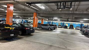 Un parking souterrain à plusieurs niveaux, avec des voitures garées dans des emplacements désignés, des piliers en béton et un éclairage au plafond.