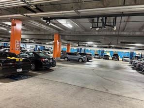 A multi-level underground parking garage with cars parked in designated spaces, concrete pillars, and overhead lighting.