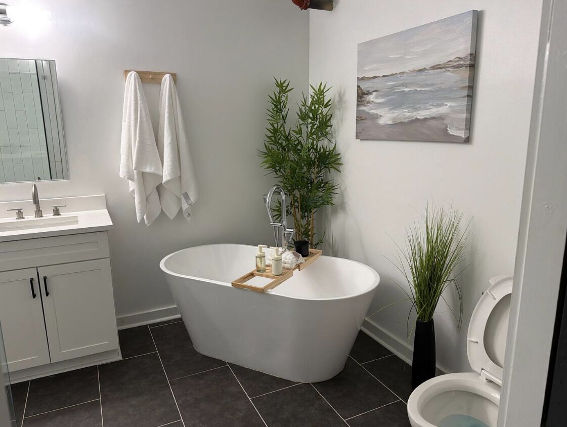A modern bathroom with a freestanding bathtub, a toilet, a sink with a mirror, and a potted plant.