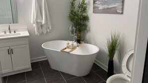 Ein modernes Badezimmer mit freistehender Badewanne, Toilette, Waschbecken mit Spiegel und einer Topfpflanze.