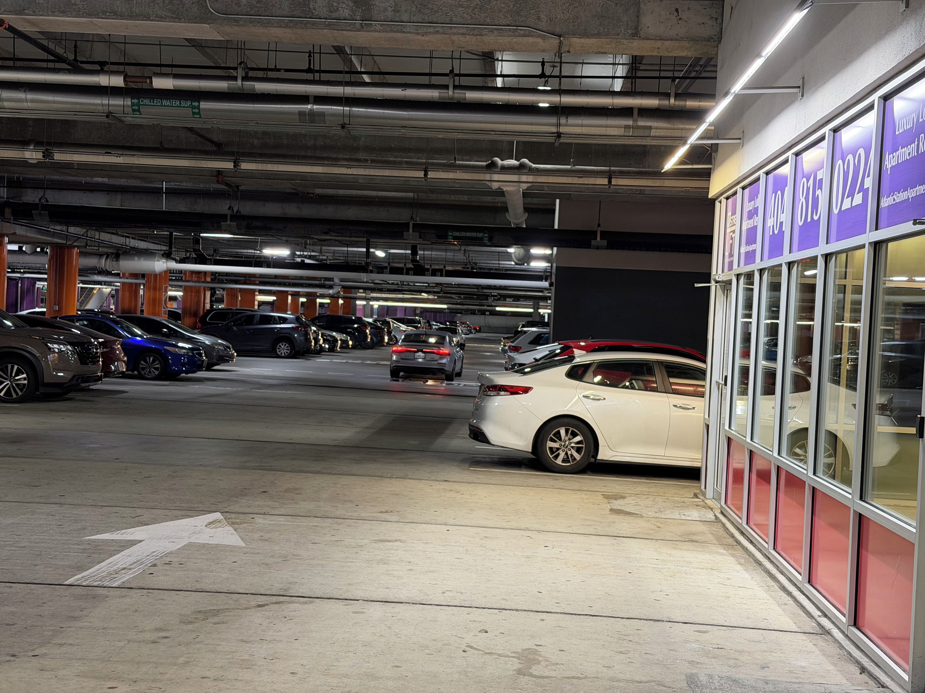 A multi-level underground parking garage with cars parked on various levels, visible structural beams, and a building with signage on the right.